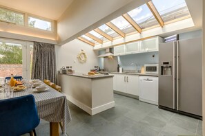 Une cuisine moderne dotée d’un îlot central, d’un coin repas avec une table dressée pour deux personnes et d’une grande verrière au-dessus.
