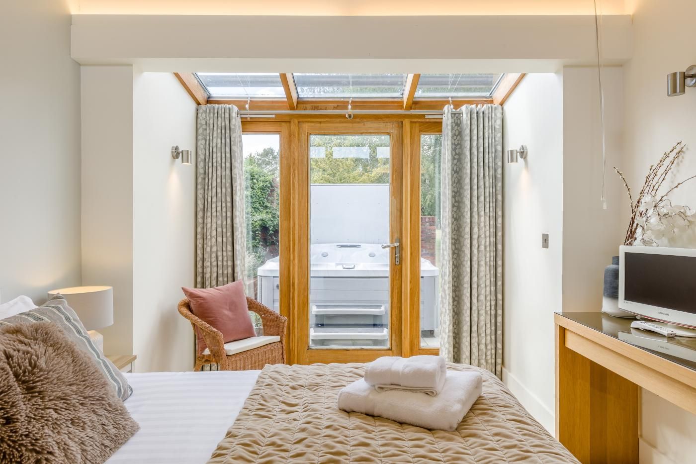 A bedroom with a bed, a chair, a TV, and a view of a hot tub through a glass door.