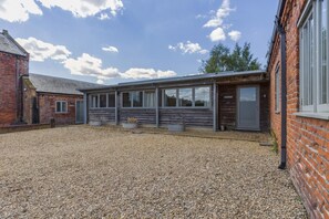 A building with a gravel courtyard, a wooden structure with large windows, and a brick wall. - 3 Bed in Cranmer (oc-g45793) (Cranmer)
