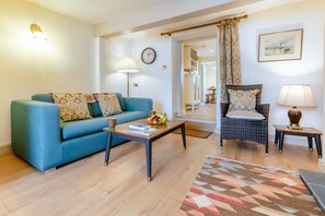 A living room with a blue sofa, a wicker chair, a coffee table, and a patterned rug. - 2 Bed in Appledore (oc-d45715) (Appledore)