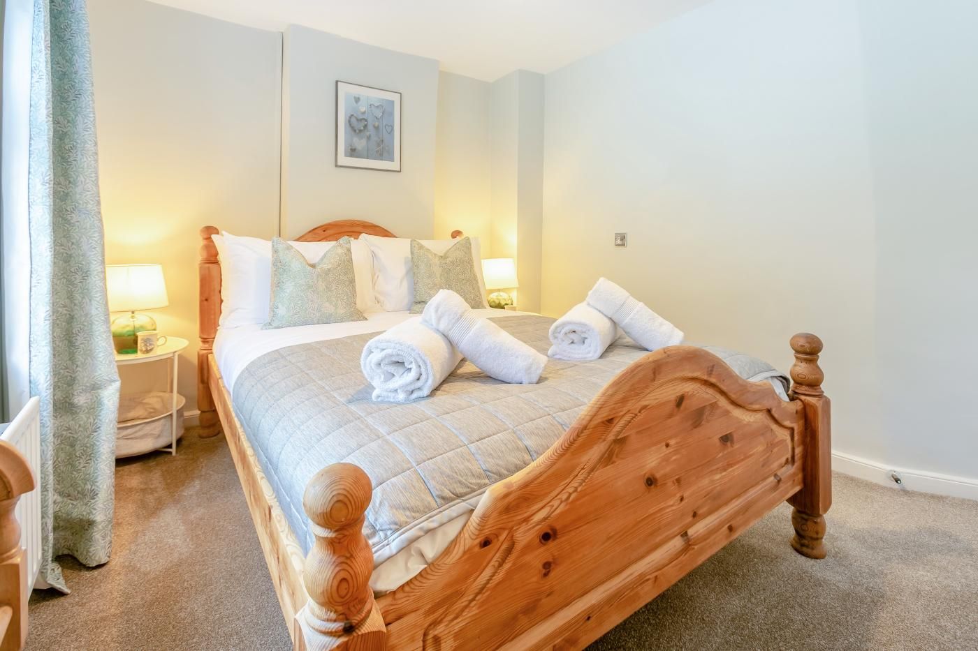 A neatly made bed with a wooden headboard, two bedside lamps, and a framed picture on the wall.