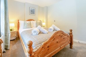 Een net opgemaakt bed met een houten hoofdbord, twee bedlampen en een ingelijst beeld aan de muur.