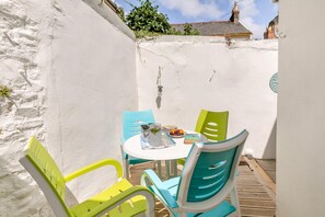 A small outdoor seating area with a round table and four chairs, a small table with a book and a glass, and a white wall with a window. - 2 Bed in Appledore (oc-d45715) (Appledore)