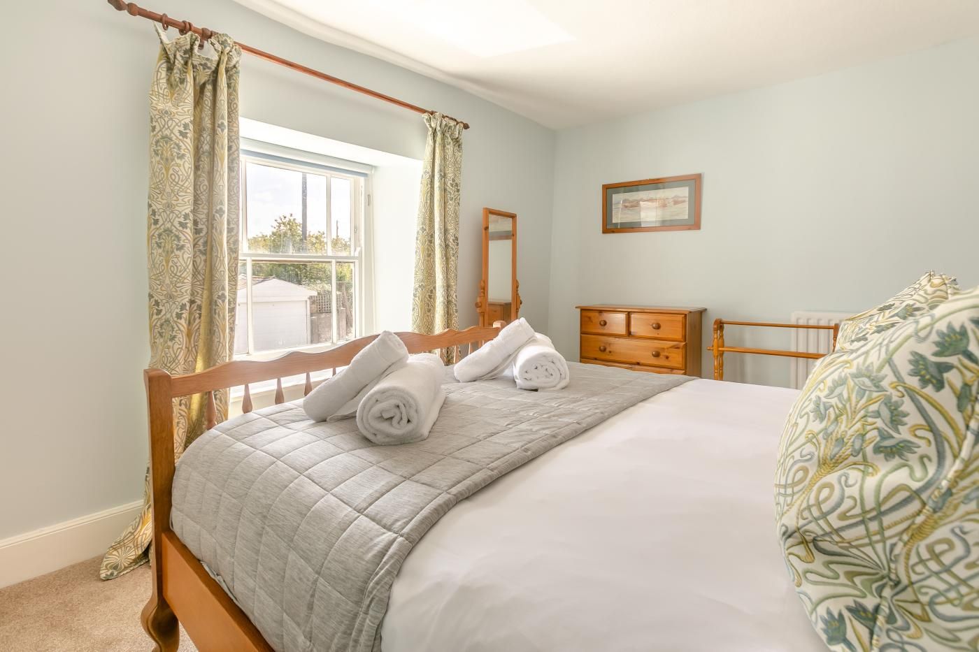 Une chambre à coucher avec un lit, une table de chevet en bois, une commode et une fenêtre avec des rideaux.
