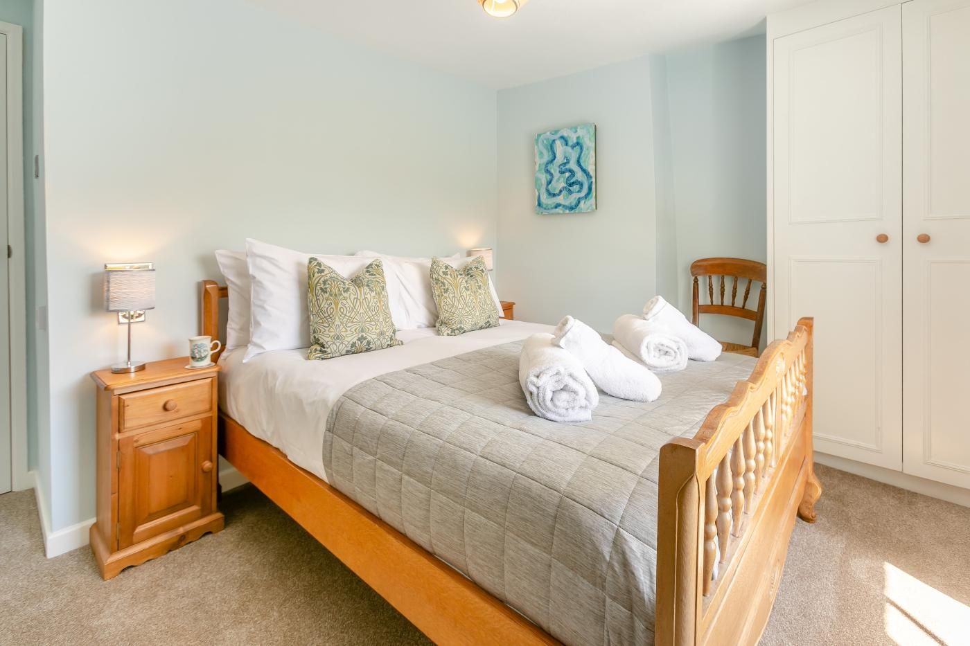 A neatly made bed with a quilted cover, a bedside lamp, and a wooden nightstand with a drawer.