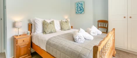 A neatly made bed with a quilted cover, a bedside lamp, and a wooden nightstand with a drawer.