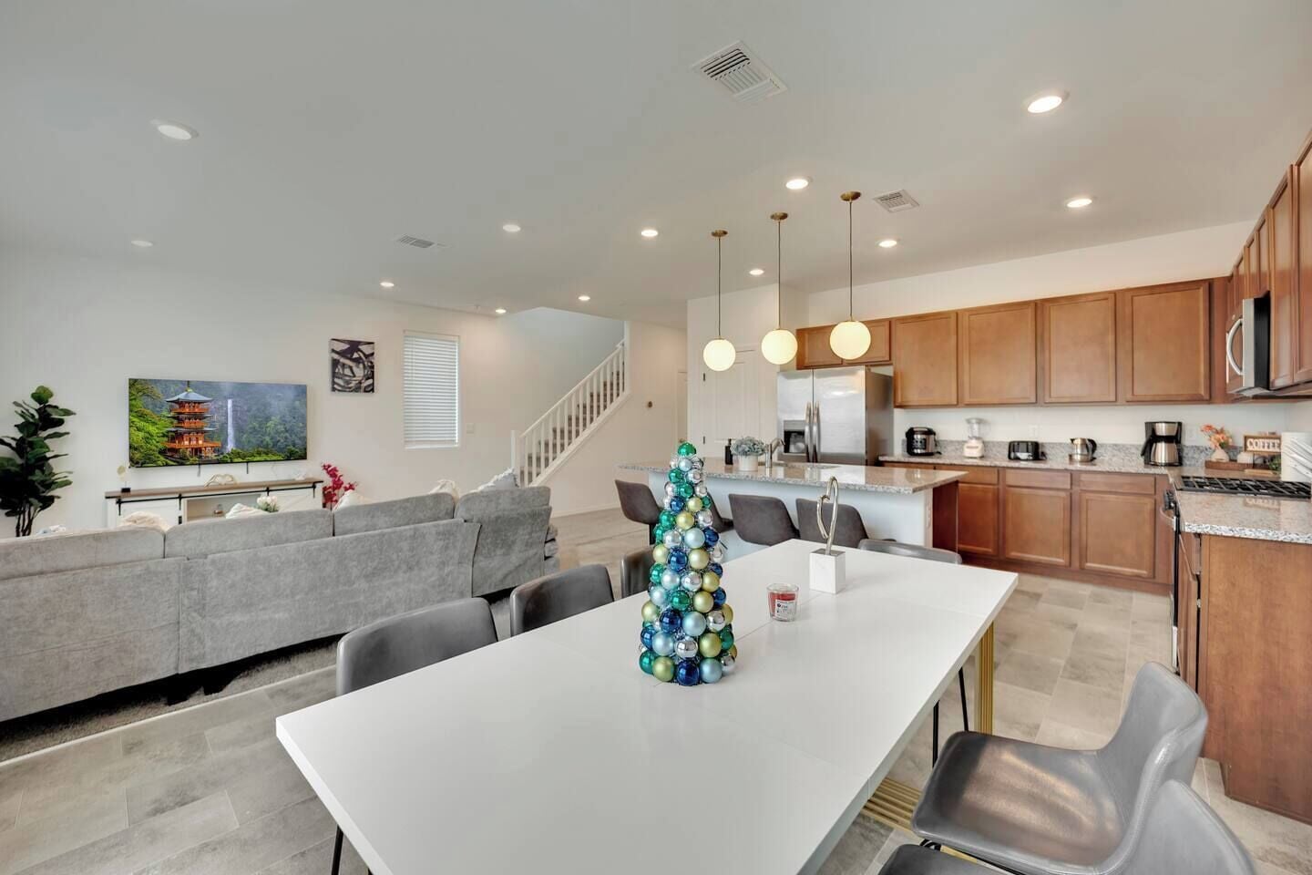 A modern kitchen with wooden cabinets, stainless steel appliances, and a dining area with a white table and grey chairs.