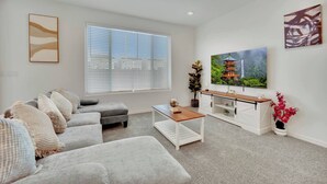 A modern living room with a grey sofa, a coffee table, a TV on a white cabinet, and a large window with blinds. - Modern 5B3B｜Near Strip｜Fiber WiFi｜TV in all Rooms (Las Vegas)