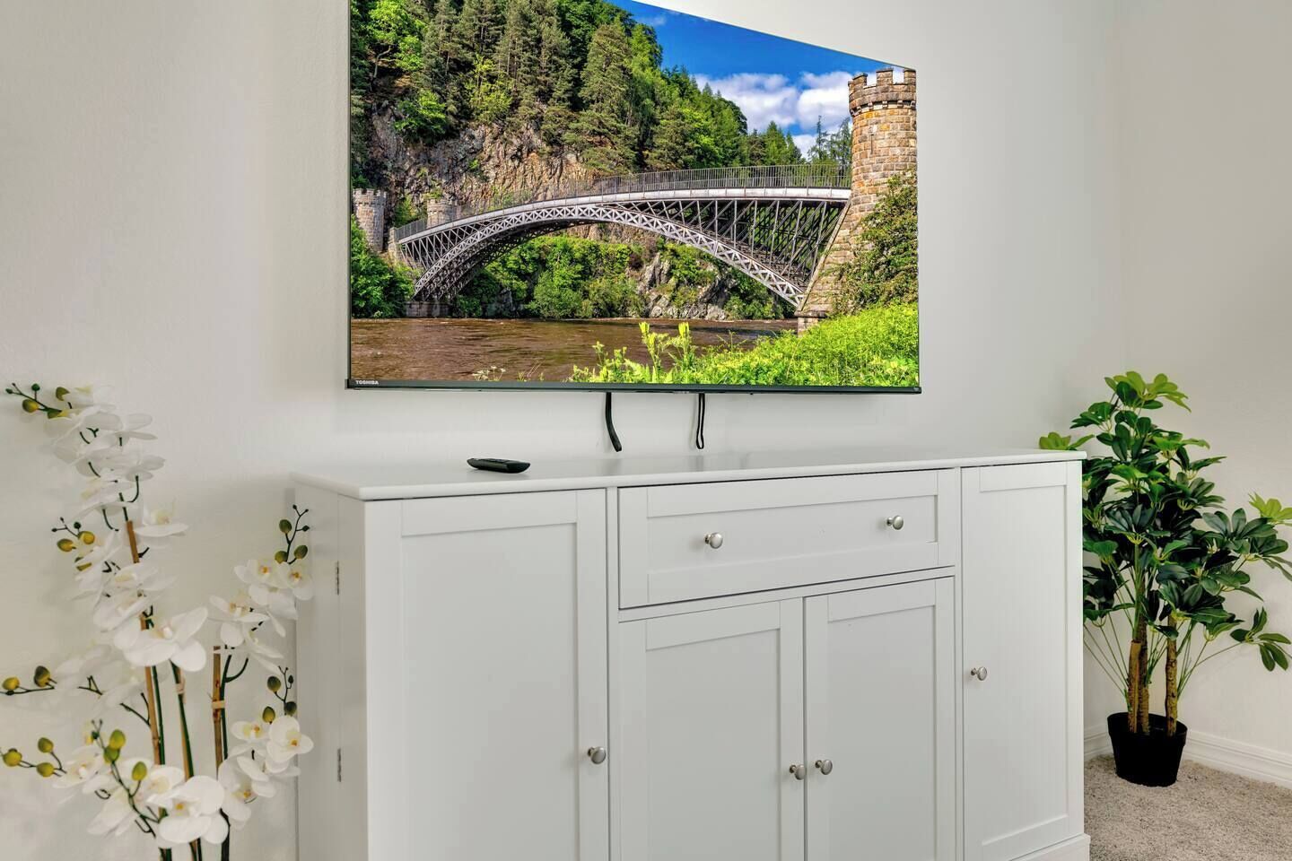 Uma central de entretenimento branca com uma televisão de tela plana montada acima, exibindo uma imagem panorâmica de uma ponte.