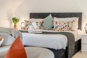 A neatly made bed with a grey headboard, white bedding, and colorful floral-patterned pillows. - 2 Bed in Weston (oc-a45906) (Weston)