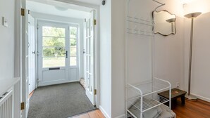 En hall med en vit dörr som leder in till ett ljust rum, ett torkställ av metall och en golvlampa.