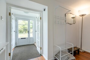 Ein Flur mit einer weißen Tür, die zu einem hellen Raum führt, einem Wäscheständer aus Metall und einer Stehlampe.