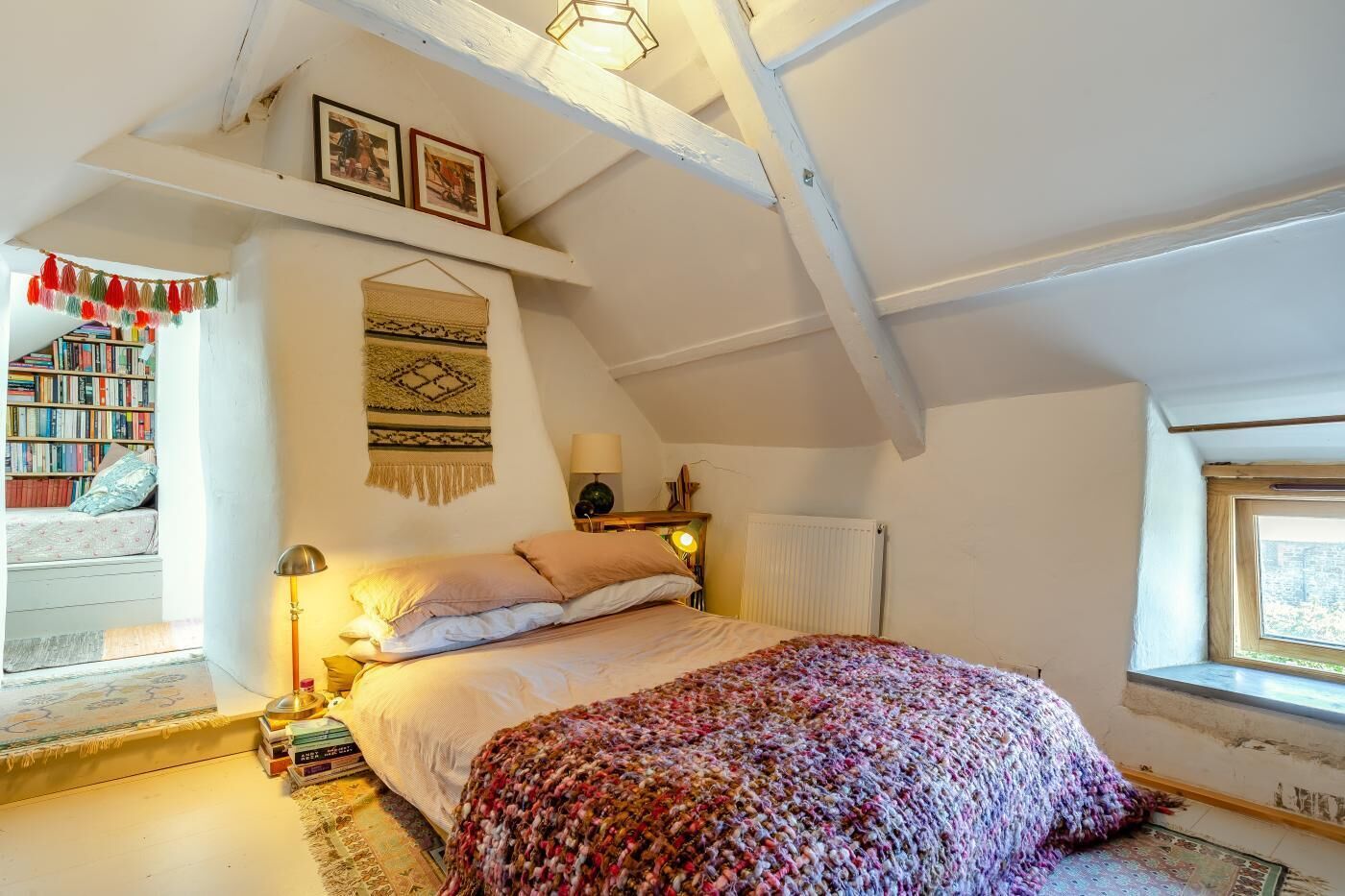 A cozy attic bedroom with a bed, a reading nook with books, and a window with a view.