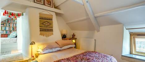 A cozy attic bedroom with a bed, a reading nook with books, and a window with a view.