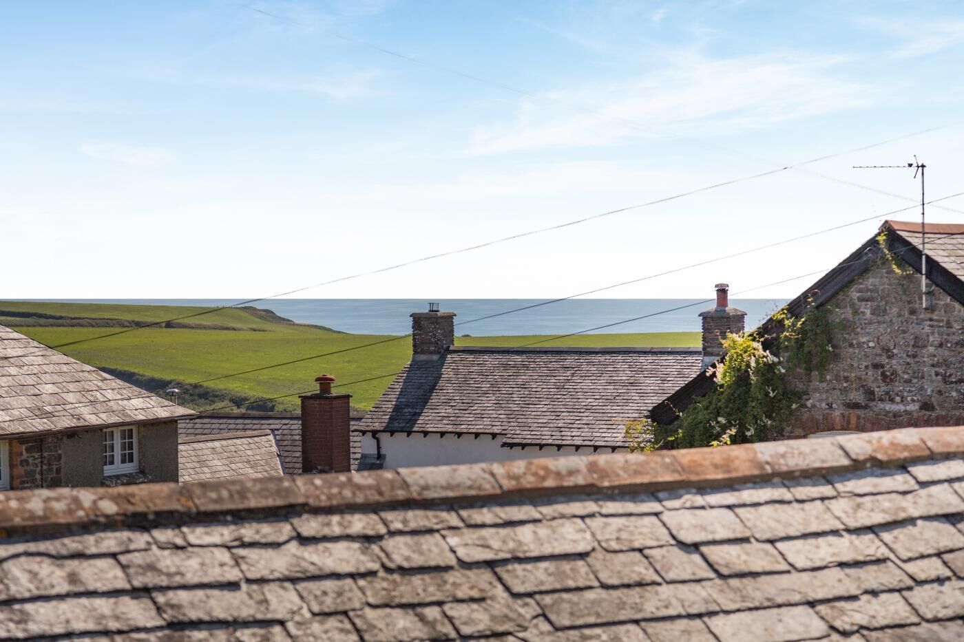 A rural landscape with stone buildings, a clear sky, and a view of the sea.