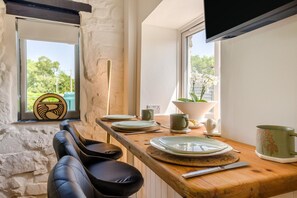 Ein Essbereich mit einem Holztisch, Stühlen und Blick ins Freie durch ein Fenster.