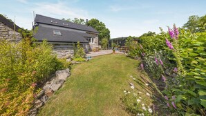 A stone house with a sloped roof, a small lawn, and various plants and flowers. - 2 Bed in Llanwrthwl (oc-b45319) (Llanwrthwl)