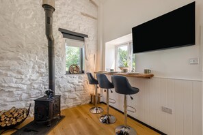 Ein gemütliches Zimmer mit Steinwand, Kaminofen, Holzboden und einer Bar mit Hockern.