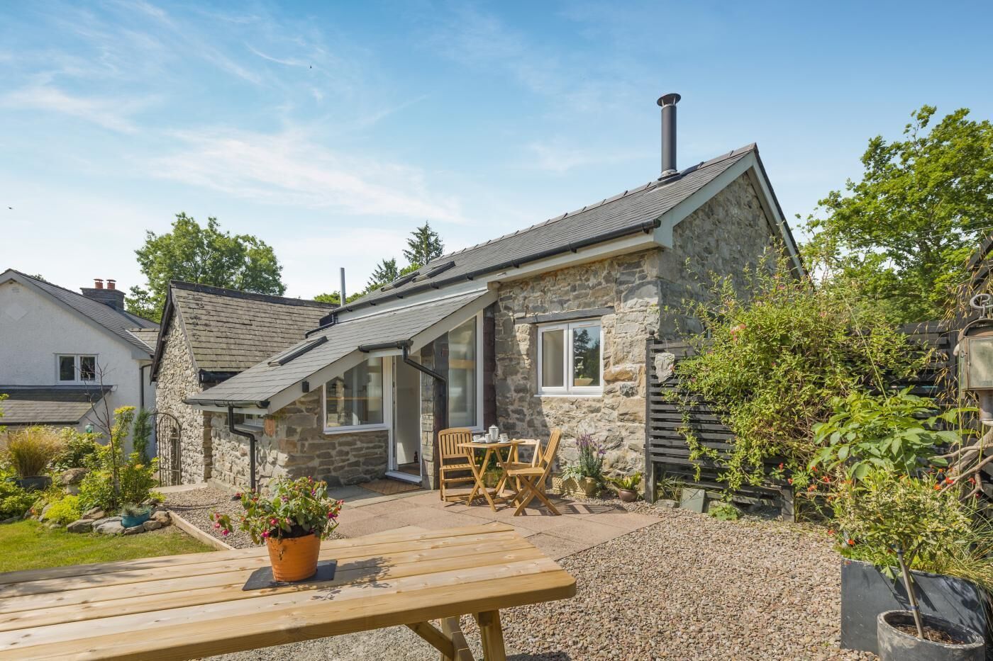 A stone house with a sloped roof, a chimney, and a patio with wooden furniture.