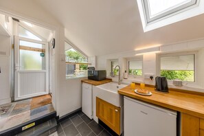 Eine kompakte Küche mit Geschirrspüler, Mikrowelle und Kaffeemaschine. Fenster sorgen für Tageslicht und einen Blick ins Grüne.