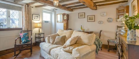 Una habitación acogedora con techo de madera, un sofá, una silla, una mesa con un florero y una ventana con cortinas.
