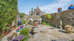 A stone building with a pointed roof, surrounded by a garden with various plants and flowers. - 1 Bed in Ribchester (oc-n45957) (Ribchester)