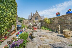 A stone building with a pointed roof, surrounded by a garden with various plants and flowers. - 1 Bed in Ribchester (oc-n45957) (Ribchester)