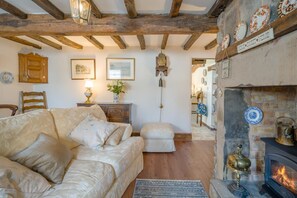 A cozy living room with a fireplace, wooden beams, a sofa, and a decorative cabinet.