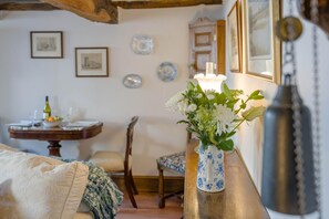 A room with a bed, a table with a bottle and glasses, a chair, a vase with flowers, and a lamp.