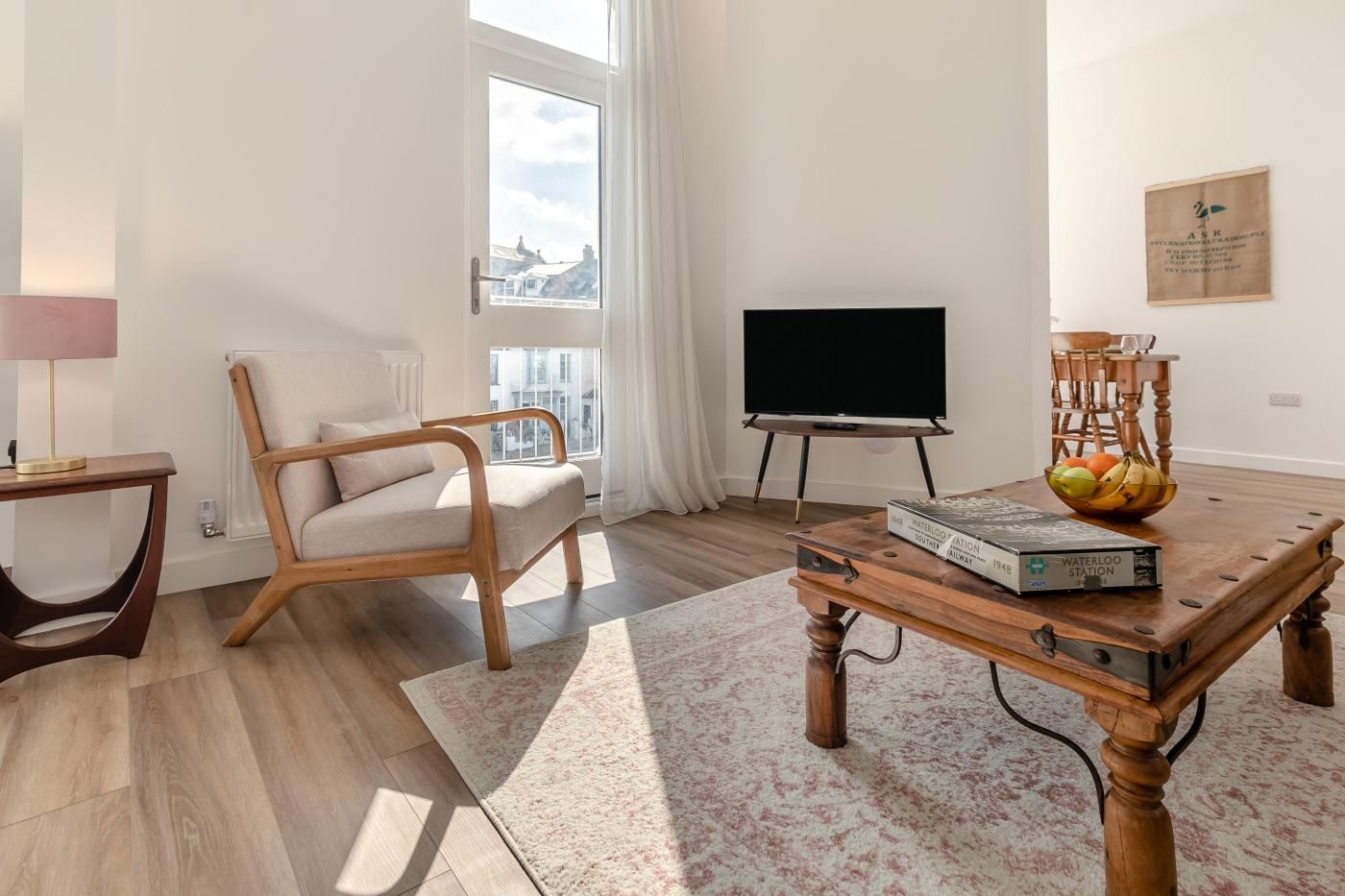 Un salon moderne avec un canapé, une table basse sur laquelle repose un livre, un téléviseur et une fenêtre donnant sur un beau paysage.