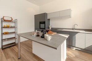 A modern kitchen with a central island, built-in appliances, and a minimalist design. - 3 Bed in Ilfracombe (oc-b45837) (Ilfracombe)