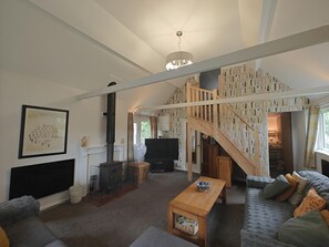 Uma sala de estar espaçosa com lareira, uma escada de madeira e um sofá aconchegante.