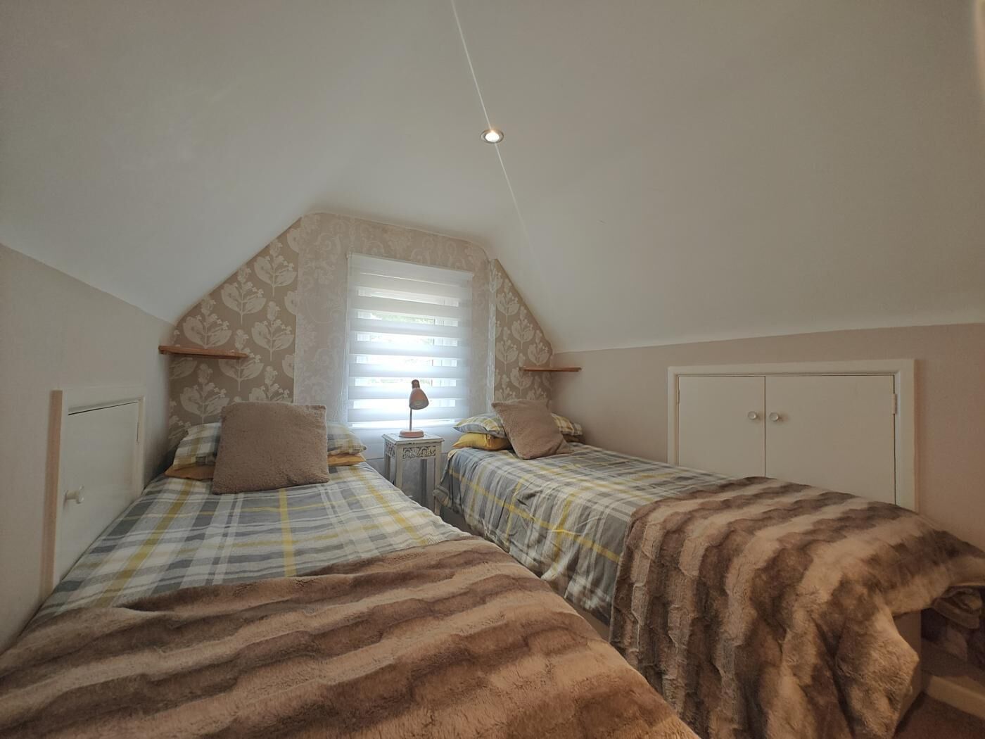 Ein Schlafzimmer mit zwei Betten, einem Fenster mit Jalousien, einer Lampe auf einem Nachttisch und einem Kleiderschrank.