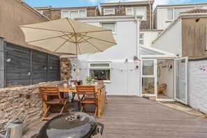 A patio with a table and chairs, a barbecue grill, and a large umbrella. - 4 Bed in Brixham (oc-a45940) (Brixham)