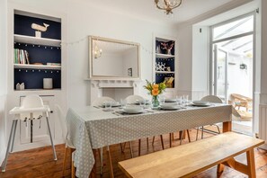 A dining area with a table set for four, a white chair, a wooden bench, and a bookshelf with decorative items. - 4 Bed in Brixham (oc-a45940) (Brixham)
