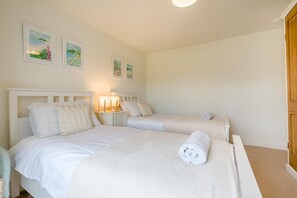 Una habitación con dos camas, cada una con cabecera, una mesita de noche con lámpara y una toalla enrollada sobre la cama.