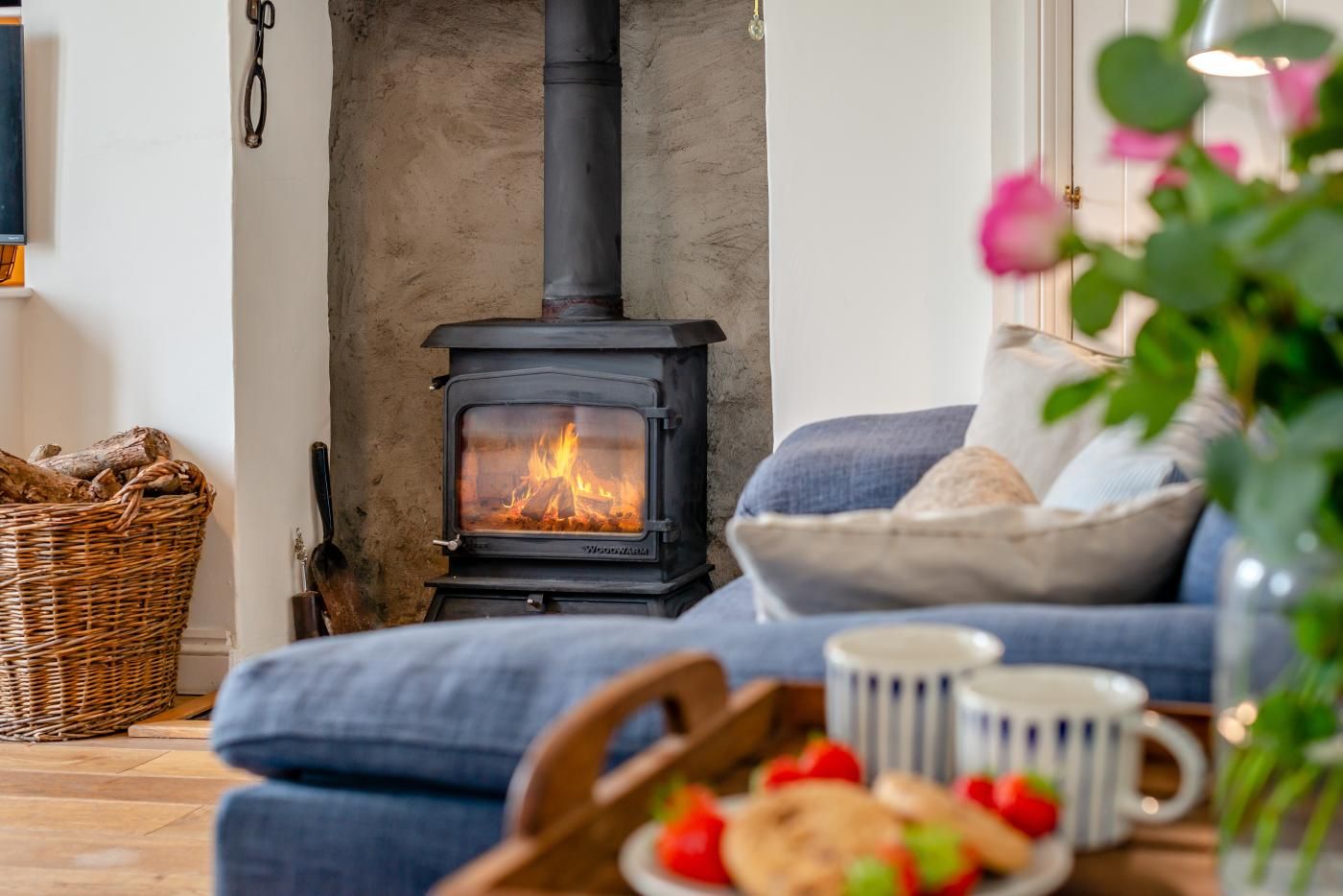 A cozy living room with a wood-burning stove, a wicker basket, a bowl of bread, and a mug on the floor.