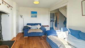 A cozy living room with a blue sofa set, a wooden floor, and a kitchen visible through an open door. - 3 Bed in Treknow (oc-p45966) (Treknow)
