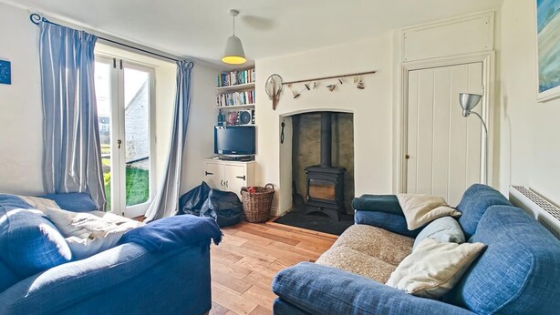 A living room with a sofa set, a fireplace, a bookshelf, and a large window. - 3 Bed in Treknow (oc-p45966) (Treknow)