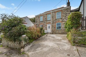 A stone house with a front door, a small porch, and a garden with flowering plants. - 3 Bed in Treknow (oc-p45966) (Treknow)