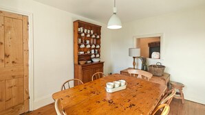 A wooden dining table with chairs, a hanging light fixture, and a cabinet with kitchenware. - 3 Bed in Treknow (oc-p45966) (Treknow)