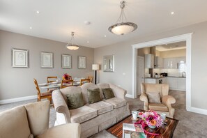 A living room with a beige sofa, a coffee table with a vase of flowers, and a dining area with a table set for four. - 2 Bed in Weymouth (oc-m45968) (Weymouth)