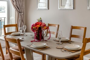 A dining table set for four with chairs, a vase of flowers, and a window with curtains. - 2 Bed in Weymouth (oc-m45968) (Weymouth)