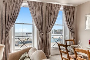 A room with a view of a bridge and water, a dining table with chairs, and a sofa. - 2 Bed in Weymouth (oc-m45968) (Weymouth)