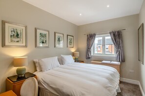 A hotel room with a large bed, two bedside tables, a window with curtains, and framed artwork on the wall. - 2 Bed in Weymouth (oc-m45968) (Weymouth)