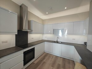 A modern kitchen with white cabinetry, a black countertop, and a stainless steel range hood. - 2 Bed in Weymouth (oc-m45968) (Weymouth)