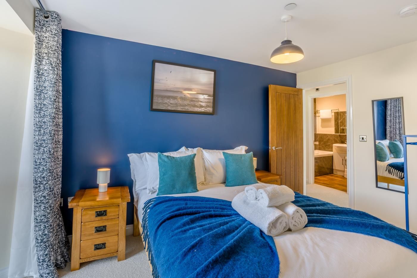 Een slaapkamer met een bed, een nachtkastje, een houten deur en uitzicht op een badkamer.