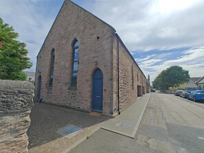 A stone building with a steep gabled roof, a blue door, and a paved street in front. - 3 Bed in Spittal (oc-b45905) (Spittal)