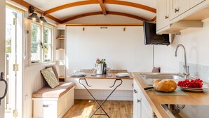 Una cocina compacta con vigas de madera, una zona de comedor con banco y un lavamanos con grifo moderno.