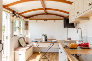 A compact kitchen with wooden beams, a dining area with a bench, and a sink with a modern faucet. - 1 Bed in St Austell (oc-h45926) (High Street)